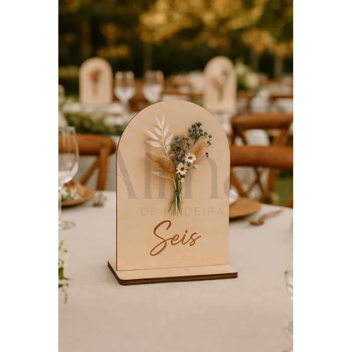 O modelo Número de Mesa Floral destaca-se pela sua base de madeira clara, topo arredondado e um arranjo de flores secas cuidadosamente colado à mão.