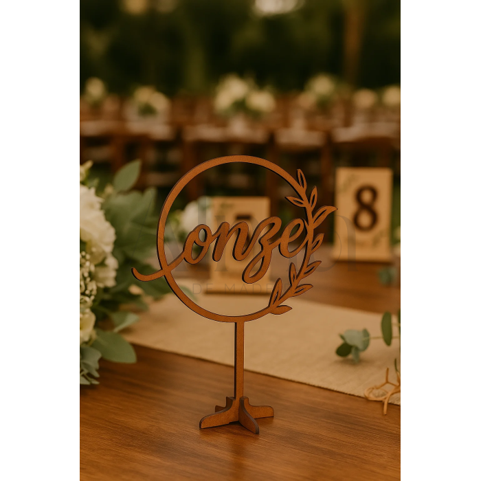 O modelo Número de Mesa Circular é feito em MDF e apresenta a palavra do número escrita em caligrafia fluída, envolta num aro circular com detalhe vegetal.